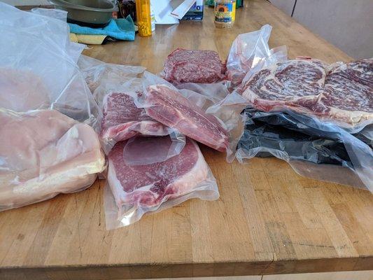 Frozen protein box with t bone steaks, hamburgers, pork chops, bone-in ribeyes, and chicken breast.