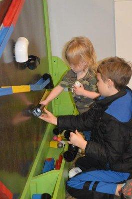 2 kiddos playing on the magnetic wall making a shute for the balls.