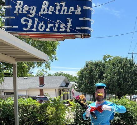 Mitch under the Rey Bethea Florist sign, trying to look serious but failing hilariously. The perfect end to a bet well lost.