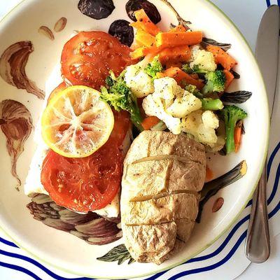 Baked cod with lemon and tomato served with a baked potato and a medley of vegetables.