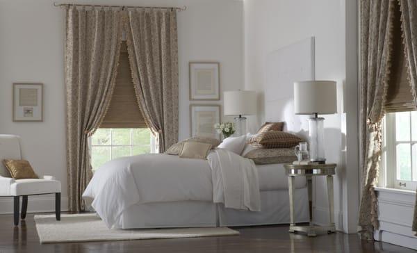 Cozy Bedroom, tall upholstered headboard, custom bedding & lots of toss pillows, drapes over a woven wood shade & a mirrored side tables