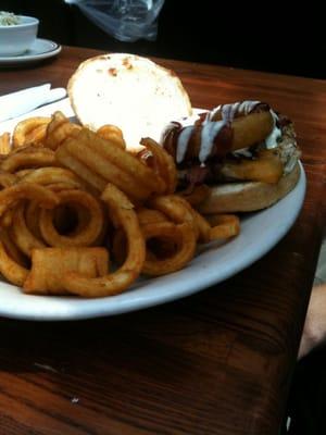 An onion ring atop a cheeseburger dripping with BBQ sauce and ranch dressing