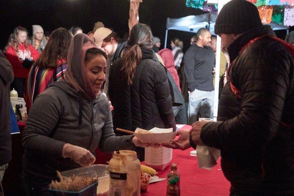 Volunteers serve elote to guests at the Mexico vista during Lanterns 2019.