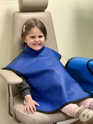 My daughter happy waiting to get her x-rays done with her stuffed animal hidden underneath the 'cape'