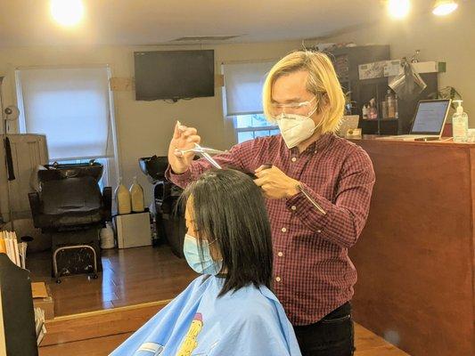 Jack  cuttingmy wife's hair, after straightening. Jack, the hairdresser, was wearing a mask and a pair of goggles.