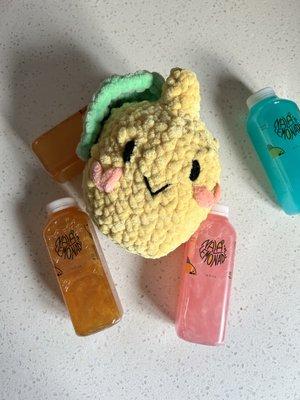 Nala's Friends Lemon Plushie surrounded by bottles of Nala's Lemonade. Glitter Lemonade