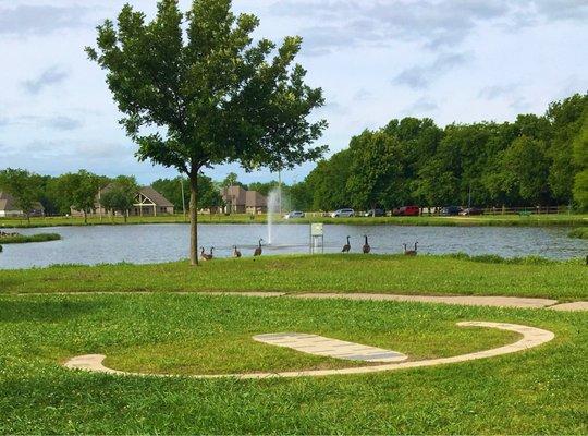 A human sundial in the foreground tells time with an adult's shadow. Lake fountain in the background.