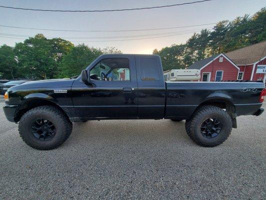 Side view of a black truck with new tires at Baldassarre Automotive, showcasing improved stance and grip.