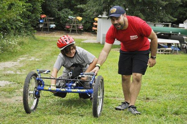 A volunteer help an athlete with trying out one of our adaptive mountain bikes.