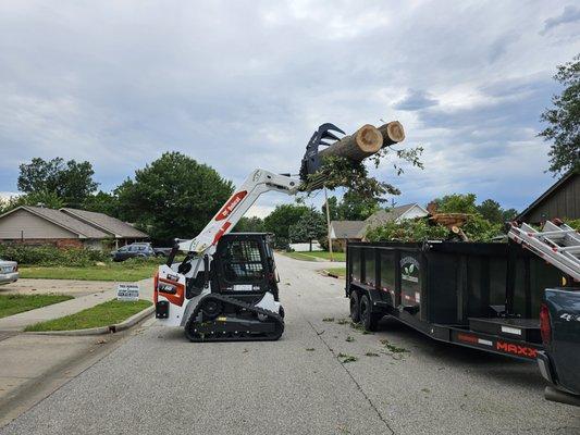 Bobcat loading trees into one of our dump trailers from a tree removal job we did in Tulsa.