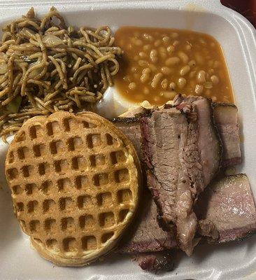 Sliced brisket on a waffle bun with garlic noodles and baked beans.