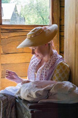 A living history volunteer works on a sewing project.