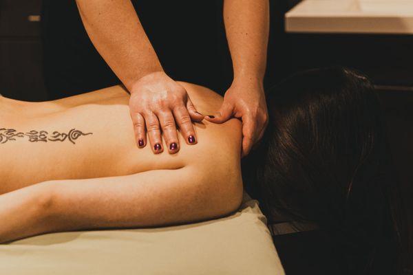 A sports massage therapist works on a client's back and shoulder.