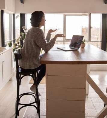 Client is having her online counseling session in her kitchen surrounded by windows.