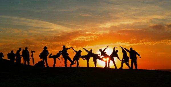 People stand together across an elevated plane with a golden sunset, as a backdrop to the blue sky, with overlapping clouds. 

Via Pexel