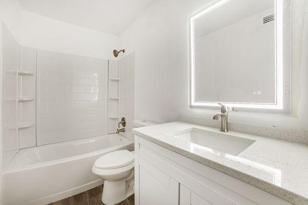 This is a picture of one of our fully renovated bathrooms. It has quartz countertops and a modern lit mirror.