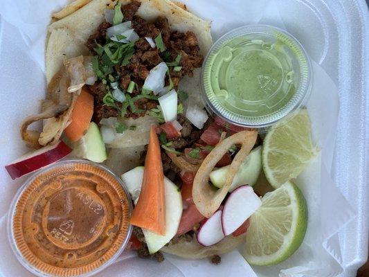 Taco al pastor and a hidden taco de carne asada with an assortment of raw and pickled veggies.