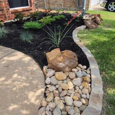 Luder stone border dressed with Colorado coble, moss boulders, seasonal plants and black mulch.