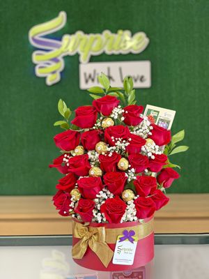 Arrangement on a round base with 24 red roses, Ferrero Rocher chocolates, foliage, card with personal message and bow.