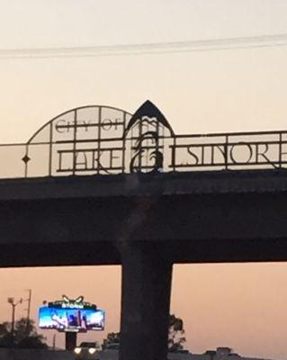 Silhouette of the ornate "Lake Elsinore" sign, on bridge over 15 Fwy.