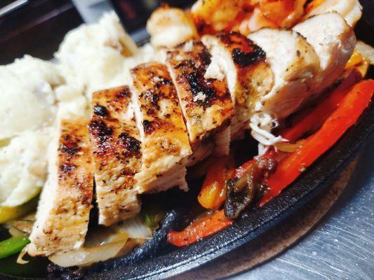 Sizzling chicken and shrimp with cheddar mashes potatoes served on a hot skillet