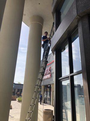 Window Technician safely using a ladder outside a storefront