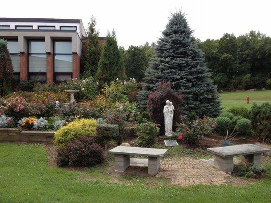 Benches in the summer garden at Notre Dame Retreat House . A quiet spot for reflection .