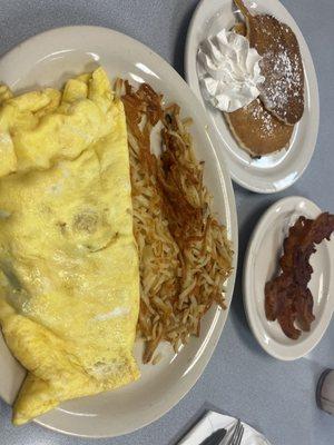 Egg omelette, hash browns, bacon strips, and chocolate chip pancakes.