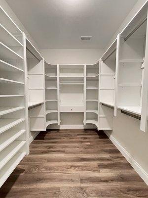 Walk-in closet with upper and lower hanging, rounded corner shelves, vanity area and shoe shelving