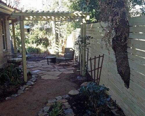 Reverse view of a sitting area and arbor with the tree carefully revealed within the fence