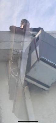 A young man hanging off the side of the roof trying to pull a 350lb boiler unit over the edge of the building (note damage to the building)