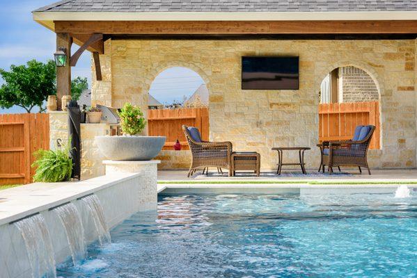 This pool area features a modern design with clear blue water and cascading waterfalls along the edge, creating a serene atmosphere. T