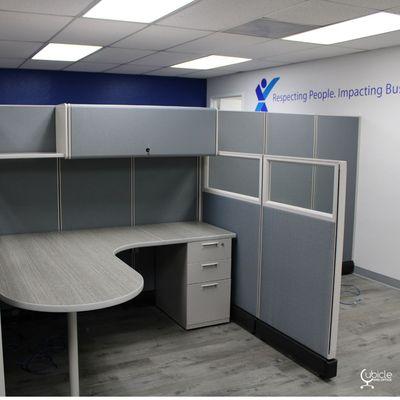 Cubicles with overhead storage and framed glass panels.