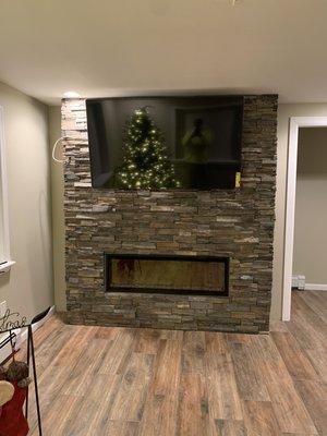 Stoned wall with electric fire place and tv on wall.