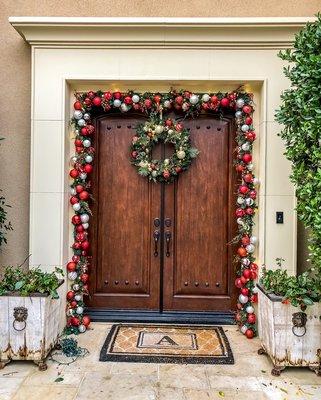 Garland trimmed around the front door with a wreath.