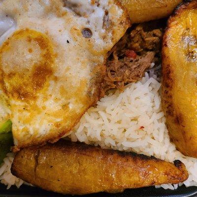 The Pabellon Criollo consists of shredded beef, white rice, black beans, fried ripe plantains, a slice of avocado, and a fried egg on top.