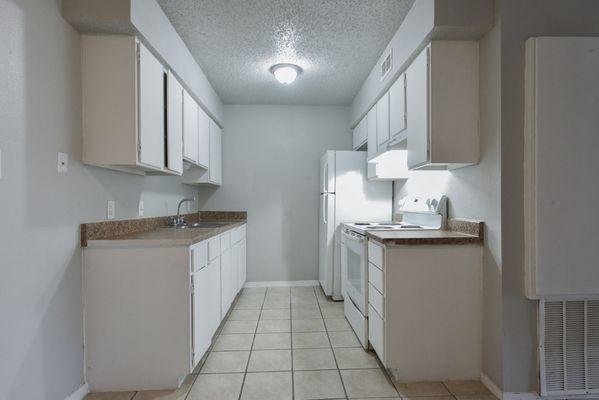 an empty kitchen with white cabinets and a white refrigerator