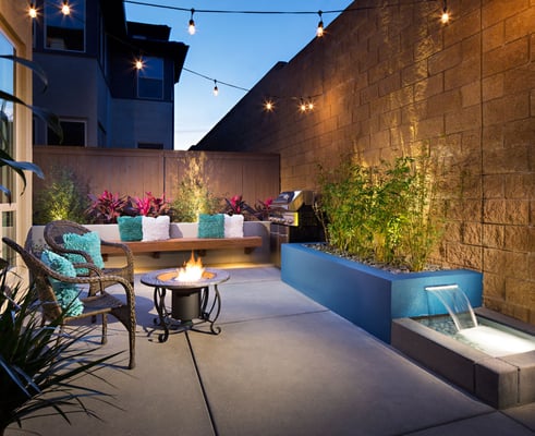 Small modern look backyard with custom water feature and wood seating bench.