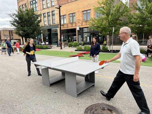 Two adults play ping pong in The Commons Pedestrian Plaza on a summer day