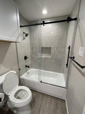 Bathroom remodel with new flooring, bath tub, sliding glass barn door, cabinets and toilet