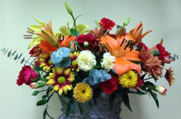 Urn with orange lilies, eucalyptus, carnations, red roses