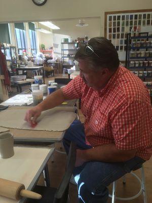 A student prepares a clay slab by smoothing the surface with a rubber rib.