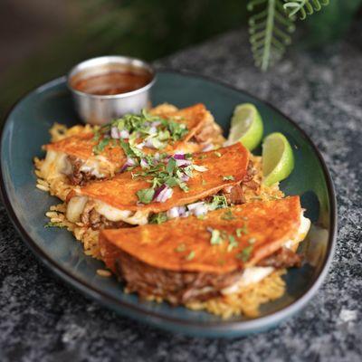 Quesabirria Tacos - Birria-style beef folded into a tortilla with melted cheese, served with a side of broth for dipping.