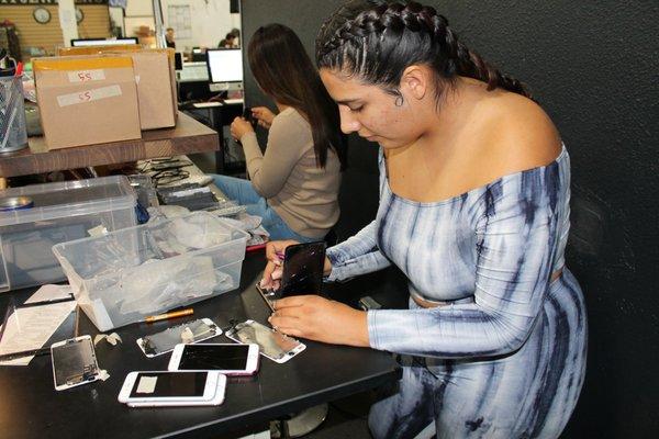 Technicians repairing an iPhone while another completes a diagnosis for a waterdamaged phone