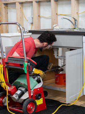 Technician cabling a sink line of a commercial property. Snake, Cable, Clog, Drains, Sewer