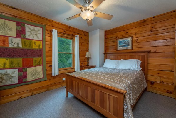 Plush bed in the Mt. Mitchell cabin bedroom, with wood panel walls and decorative quilt wall hanging