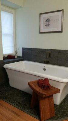 Newly installed freestanding bathtub, including new tile, stone flooring, waterfall tub filler and preservation of pre-existing wood floor.