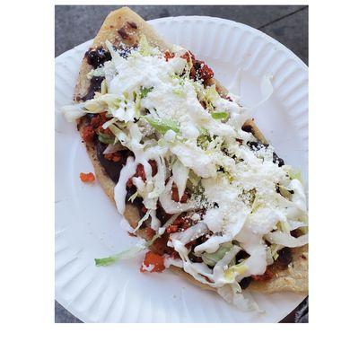 Tlacoyo de Frijoles: football-shaped corn dough patty topped with beans, chicken, lettuce, cream, and hot sauce. (Made by LaGuerreraMex)