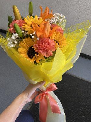 A wrapped bouquet of orange lilies and yellow sunflowers and more.