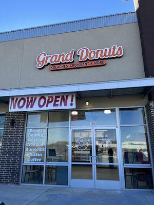 Outside Grand Donuts with a "Now Open!" Sign